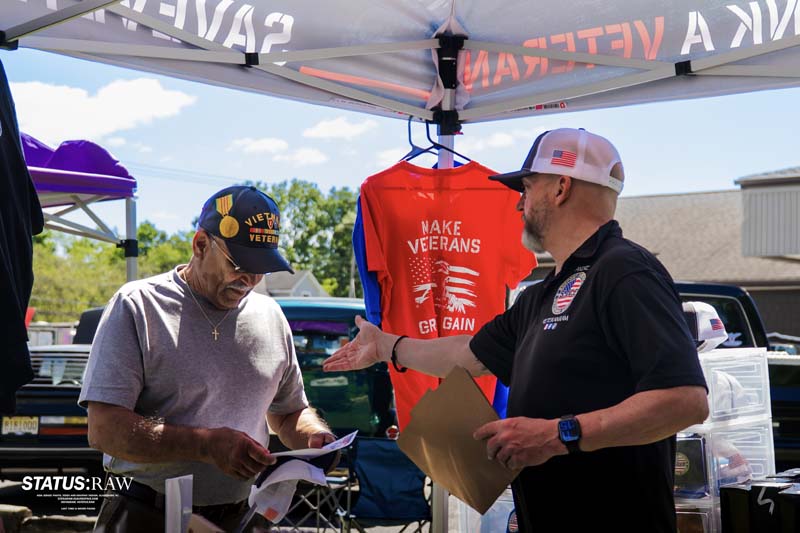 Two people interacting at booth with veterans support sign and t-shirt