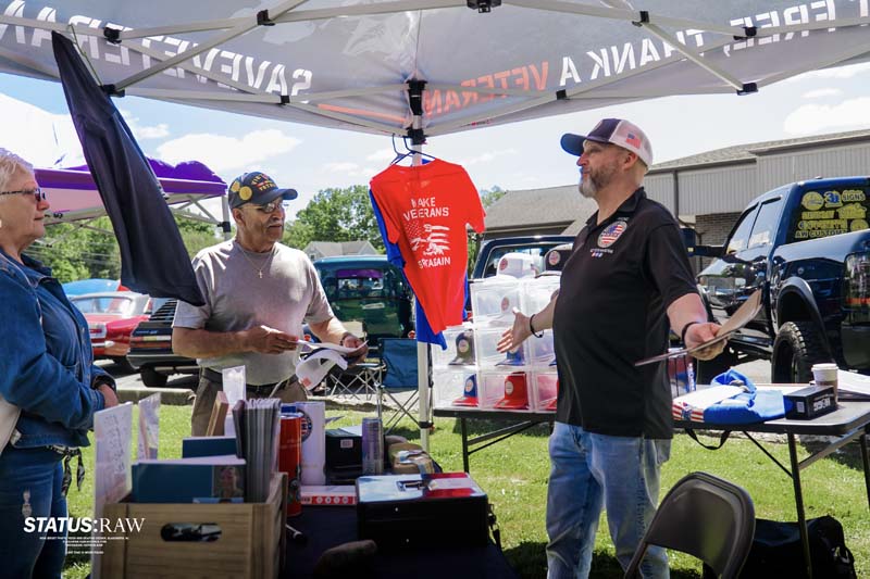 People discussing at outdoor stand with flyers and veterans shirt display