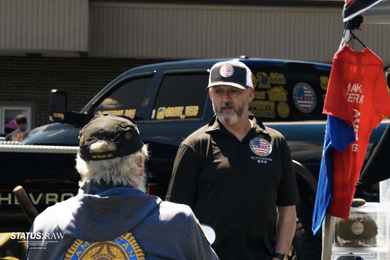 Conversation at booth with truck and veterans shirt in background