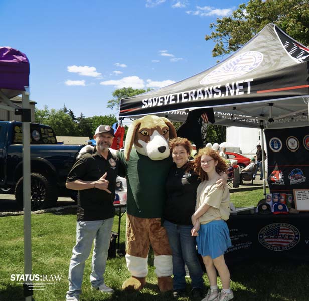 Group posing with dog mascot under veterans event tent