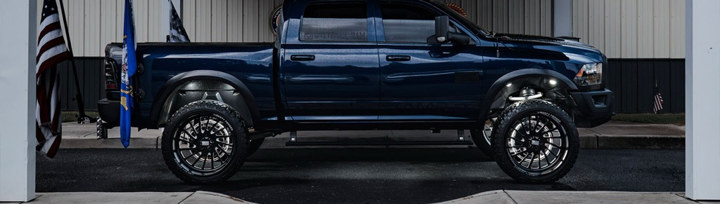 Side view of lifted blue Ram Warlock truck with flags.